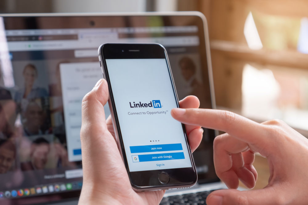 A hand holding a phone looking at the LinkedIn login screen